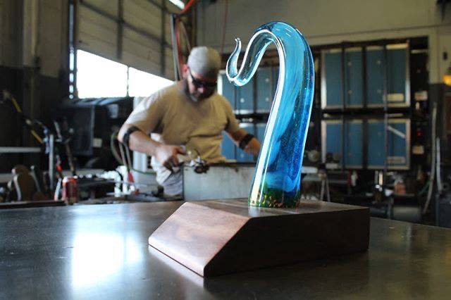 custom glass award and base in foregroun with artist working in background