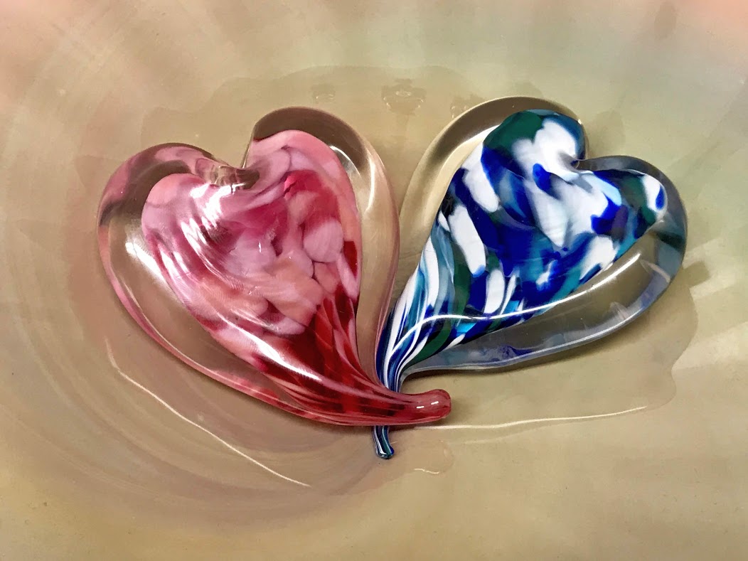 Two sculpted glass hearts, with their heart tails overlapping on a neutral background