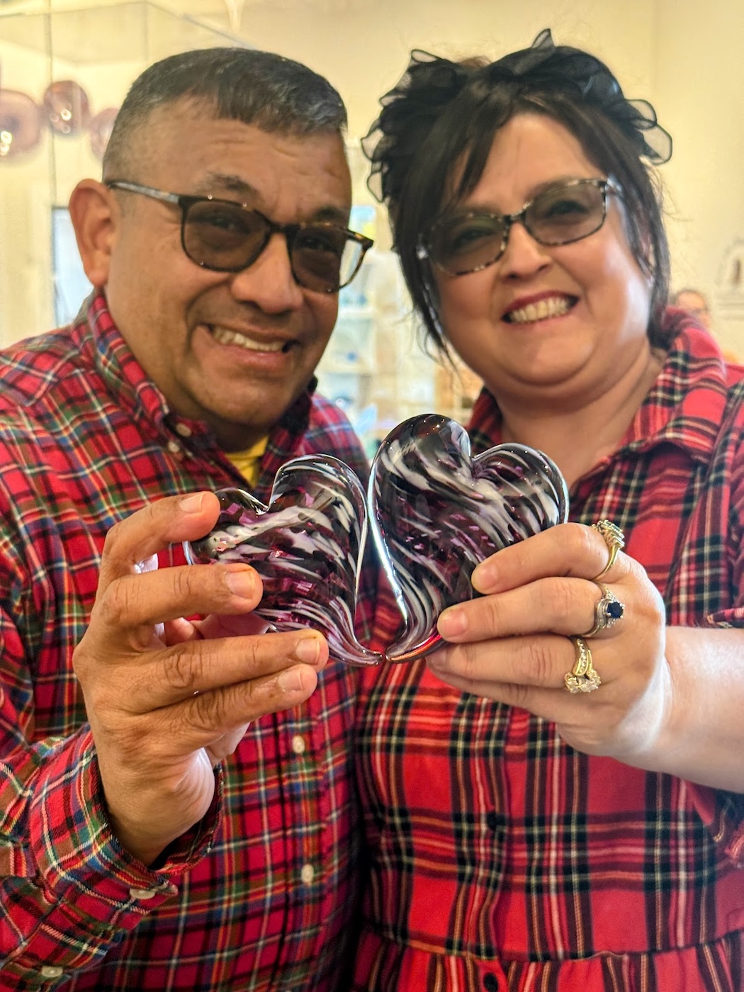 couple wearing matching plaid shirts, proudly displaying the matching red hearts they just made